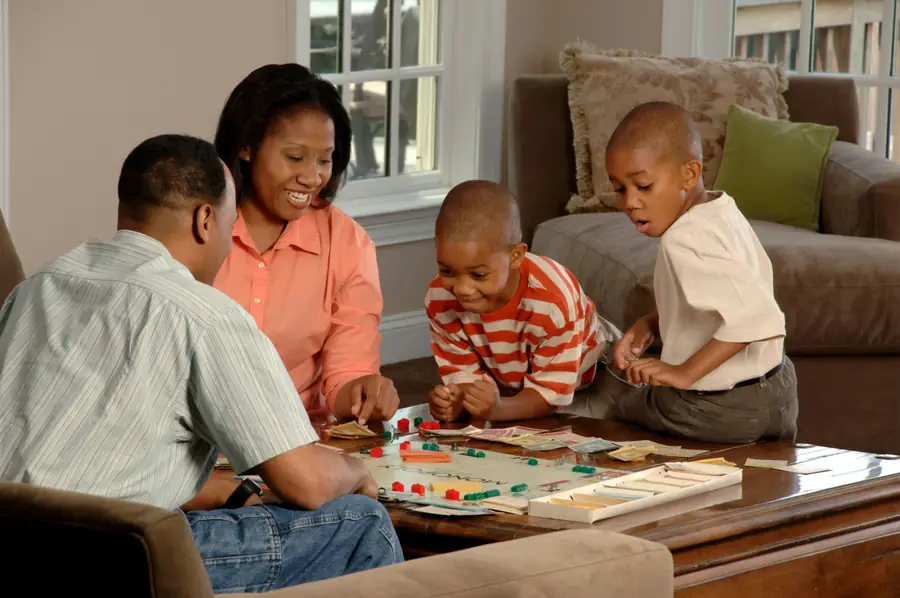 A smiling Black family of four playing a board game together in their living room